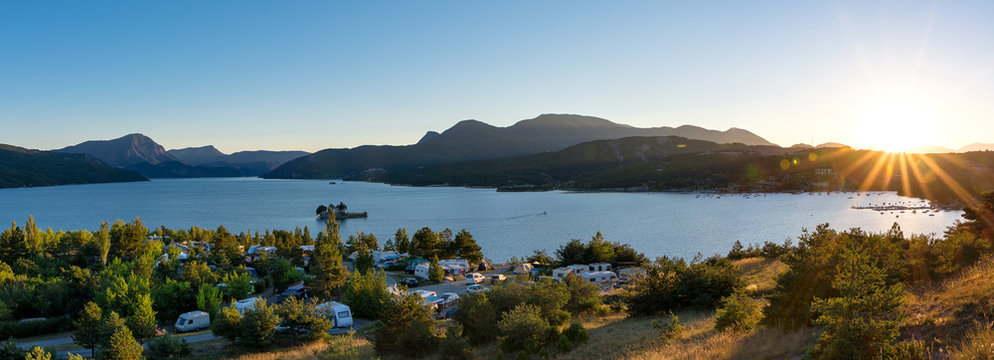 Panoramic view of the lake Lac de Serre Poncon in the French Alps and a campsite with sunset