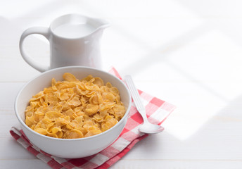 Corn flakes with jug of milk on table wooden,shadows from a window frame