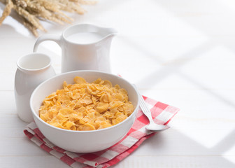 Corn flakes with jug of milk on table wooden,shadows from a window frame