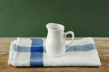 White jug and dishcloth on old wooden table over green background