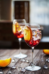 refreshing red cocktails with orange isolated on a wooden background with oranges and ice against big window