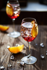 Two refreshing red cocktails with orange isolated on a wooden background with oranges and ice with backlight