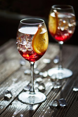 Two refreshing red cocktails with orange isolated on a wooden background with oranges and ice with backlight