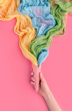 Ice cream cone in womans hand with colorful streamers  on pink background. Flat lay