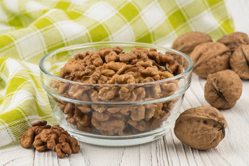 Walnuts in a glass bowl on an old white wooden table.