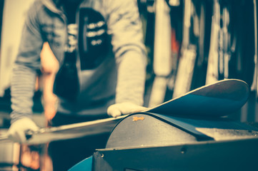 Snowboard tuning and reapairs. Winter shop worker doing base repair © guruXOX