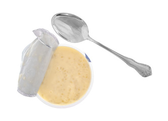 Tapioca pudding in a container with a spoon to the side and the tinfoil lid peeled back isolated on a white background.