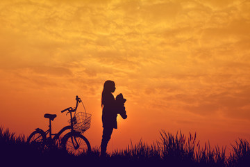 Obraz premium Silhouette of girl with bicycle on grass field at the sky sunset, color of vintage tone and soft focus concept journey