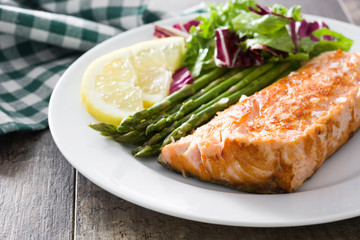 Grilled salmon fillet with asparagus and salad in plate on wooden table

