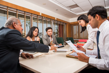 Combining their expertise. Young and good looking Indian businessman and woman gesturing and discussing something with coworkers while sitting at the office table, selective focus
