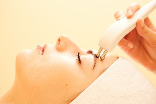 Cosmetology. Beautiful Woman At Spa Clinic Receiving Stimulating Electric Facial Treatment From Therapist. Closeup Of Young Female Face During Microcurrent Therapy. Beauty Treatment.