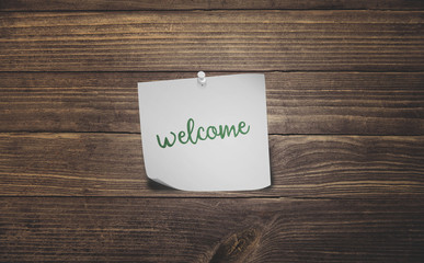 word welcome on white sticky note paper on vintage rustic wood planks floor