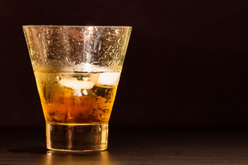 Glass of whiskey with ice cubes  on black table and background