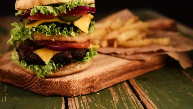 Fresh homemade beef double cheeseburger with cheese, vegetables, tomatoes, salad lettuce, onion, spicy tomato sauce and potato slices on wooden rustic background