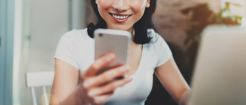 Young smiling Asian woman spending rest time at home and using smartphone for texting with friends.Selective focus. Blurred background, flares effect, wide.