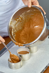 The cook pours the dough into forms for making cupcakes