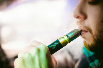 young vaper man with beard vaping mechanical mod. Guy smokes an electronic cigarette by blowing a...
