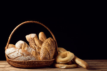Composition with bread and rolls in wicker basket isolated on wooden table