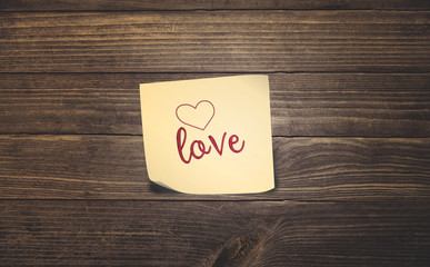 word love and heart outline on yellow sticky note paper on vintage rustic wood planks floor