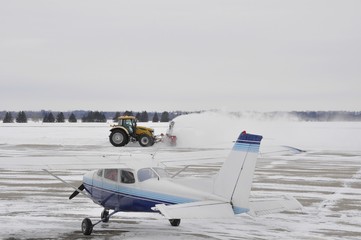 small propeller aircraft stationary on the taxiway while a snow plow is removing snow