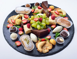 Assorted sweets, lot of sweets, cakes, fruit and chocolate on a slate base. Isolated. The concept for a restaurant.