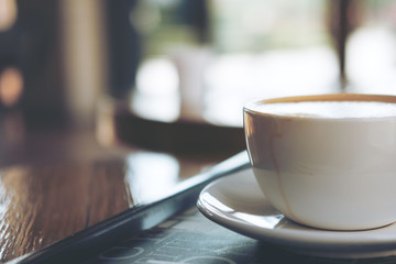 A cup of hot latte coffee on vintage wooden table in cafe with blur bokeh background