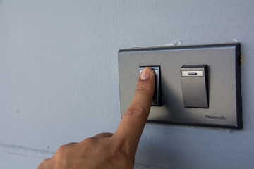 man hand with finger on light switch turn on turn off lights. Save the earth concept.