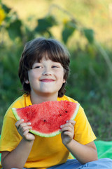 Happy child eating watermelon in garden. Boy with fruit outdoors park.
