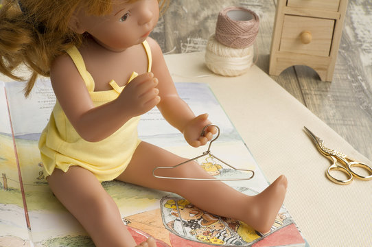 Doll in yellow suits with metal hanger is on the opened book.