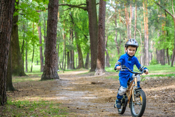 Fototapeta premium Happy cute blond kid boy having fun his first bike on sunny summer day, outdoors. child making sports. Active leisure for children. wear safety helmet. is smiling and cicling