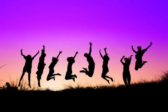 Silhouettes of young group of people jumping on the hill