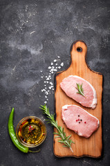 Raw meat with herbs, oil and spices on dark background with copy space. Raw pork steak. Cooking meat. Top view