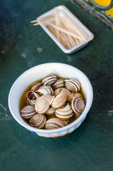Isolated boiled or cooked snails with striped shells in smaall bowl with toothpicks on table, Marrakesh, Morocco