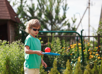 Cute boy wearing  sunglasses plays beach tennis in the garden