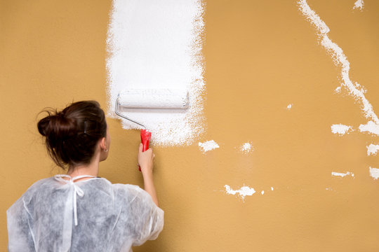 Frau streicht eine braune Wand weiß, Umbau und Renovierung