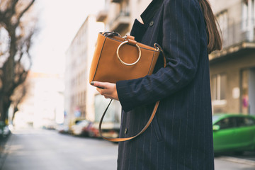 detail of a fashionable woman wearing a navy blue oversized coat and a brown trendy handbag....