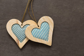 zwei Herzen aus holz mit blauem Stoff hängend vor dunklem Hintergrund