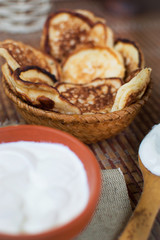Cooked homemade pancakes on a dining table in a wicker plate next to sour cream for breakfast. Sweet dessert. Homemade cooking. With your own hands. Homemade