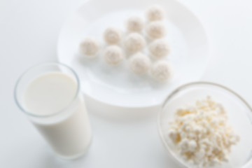 Obraz na płótnie Canvas Defocused Milk in a glass, Raffaello sweets in a bowl, on a white table, in a high key