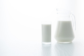 Milk in a glass and jug, on a white table, in a high key, close-up with place for text