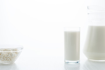 Milk in a glass and jug, cottage cheese in a bowl, on a white table, in a high key, with space for text