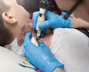 The tattoo artist makes a tattoo on the client's neck in the tattoo salon. The master does a tattoo...