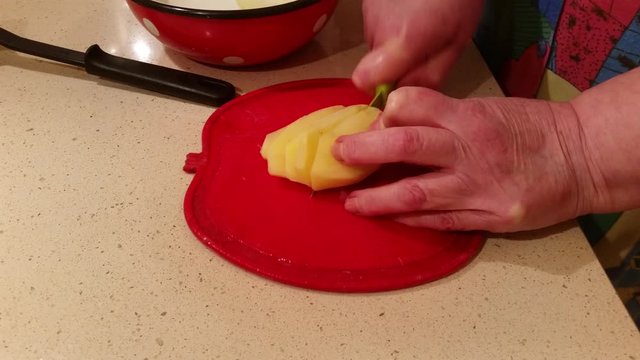 The hands of an elderly woman with a knife are chopped fresh potatoes