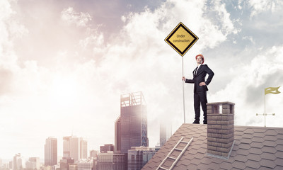 Young businessman on house brick roof holding yellow signboard a