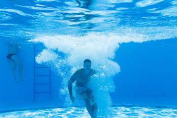 Fototapeta premium Underwater fun. Young handsome man swimming underwater and diving in the swimming poll. Sport and leisure.