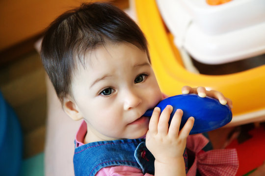 Cute infant child baby girl toddler sitting and eating blue toy