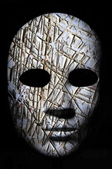 Textured mask with cracked rough wood  painted surface, neutral expression on dark background.