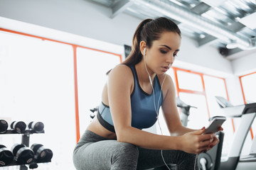 Young woman with earphones listening to music after hard workout in gym.
