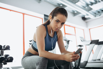 Young woman with earphones listening to music after hard workout in gym.