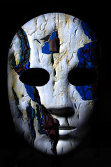 Textured mask with cracked rough wood  painted surface, neutral expression on dark background.